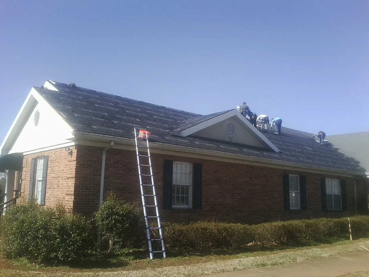Crew tearing shingles off a brick ranch roof with a ladder set — Emergency Roof Repair work by our crew in Palmyra
