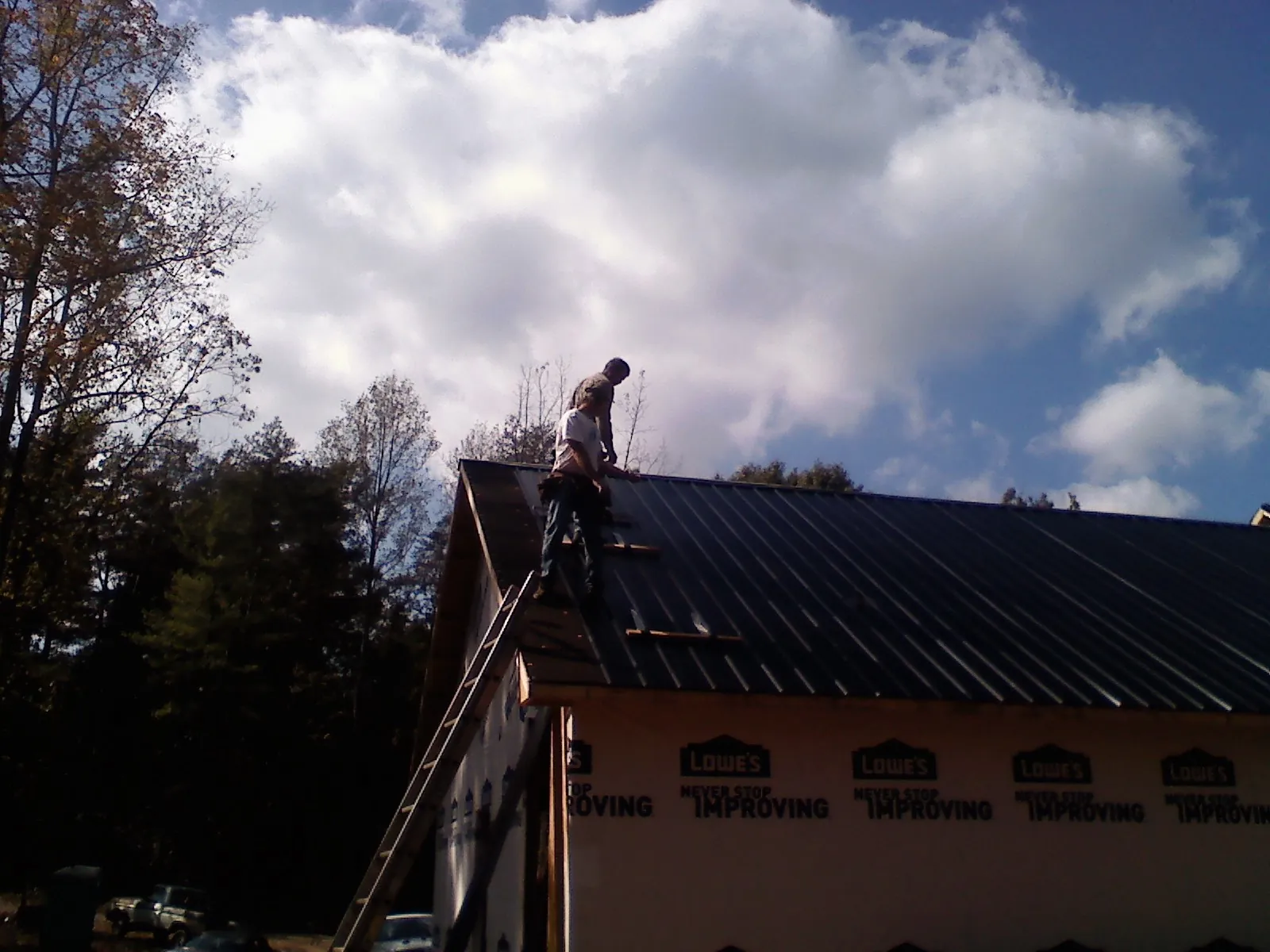 Roofer fastening dark metal panels high against a cloudy sky, from a Roof Inspection job in Palmyra